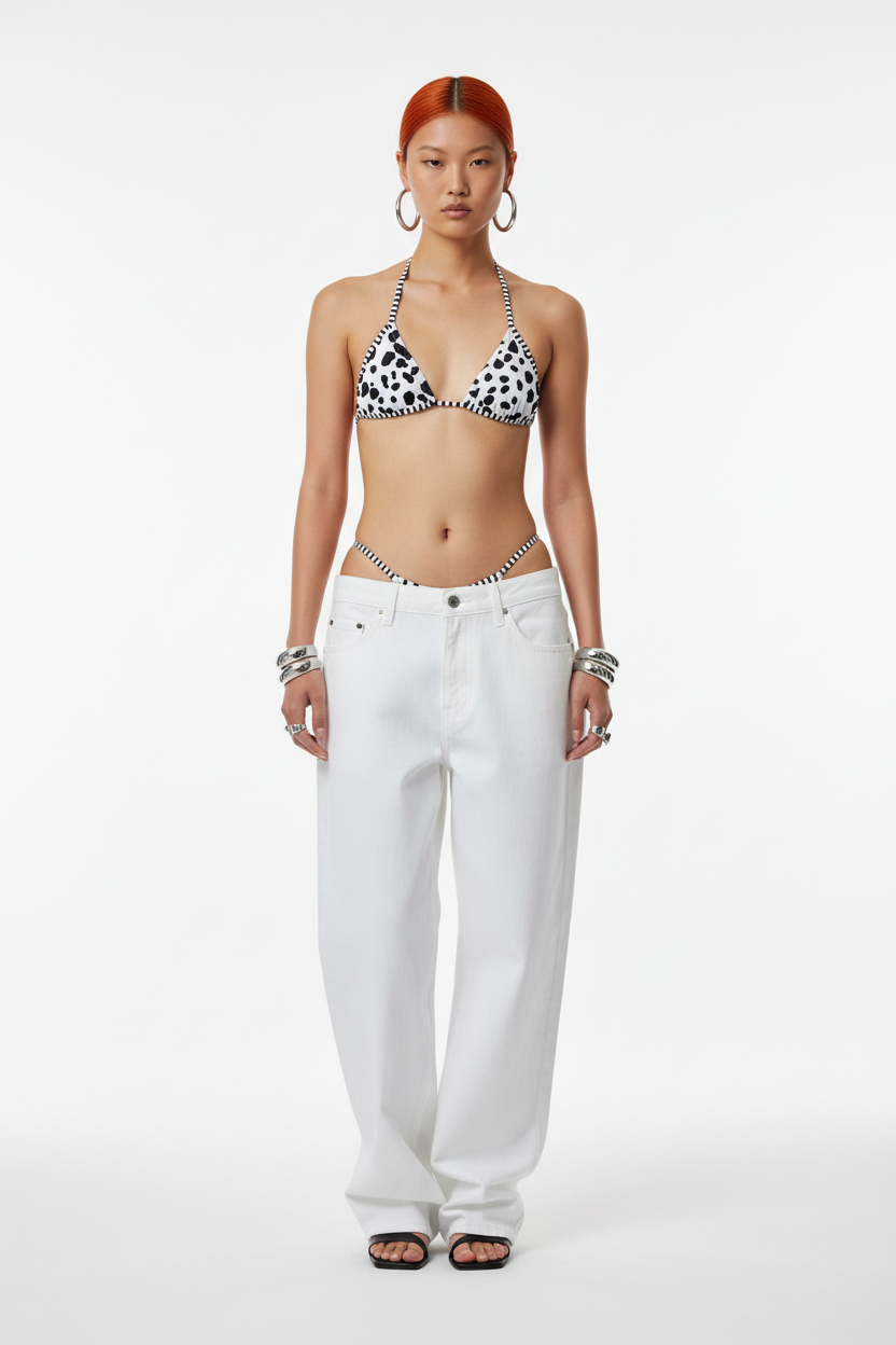 Woman wearing a black and white patterned bikini top with white pants on a white background